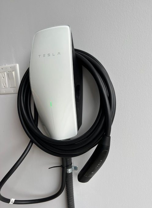 A tesla charger is attached to a wall with a black cable.
