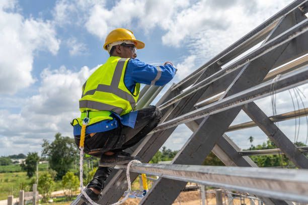 Construction worker in yellow helmet and vest on a roof, attaching something with safety harness.