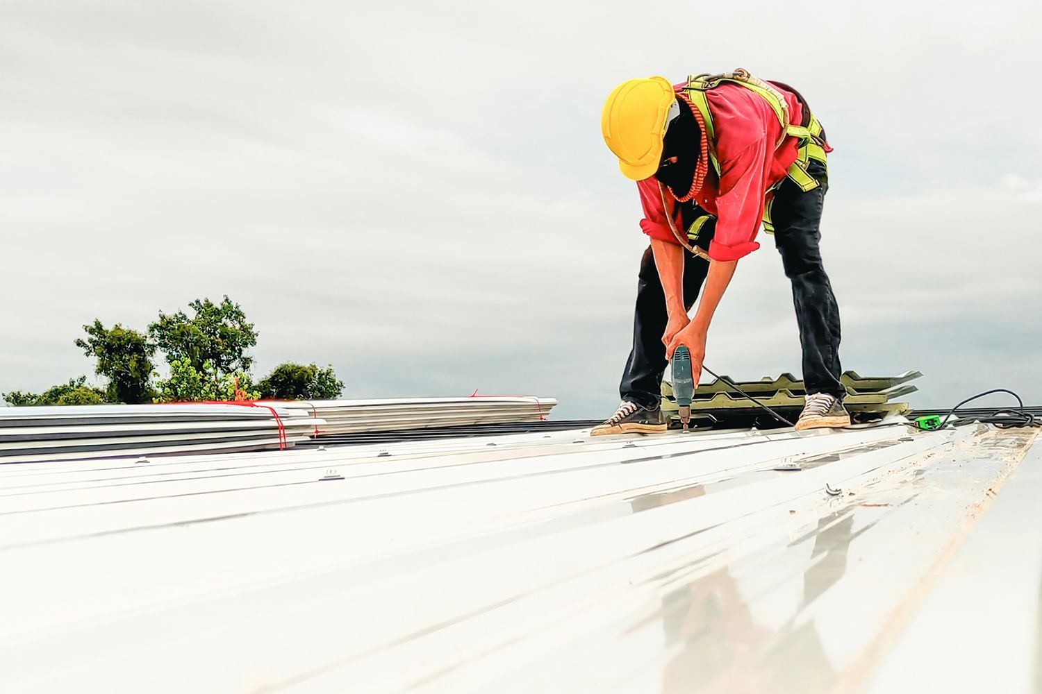 A commercial roofing contractor wearing a yellow helmet and protective gear replaces roof plates.