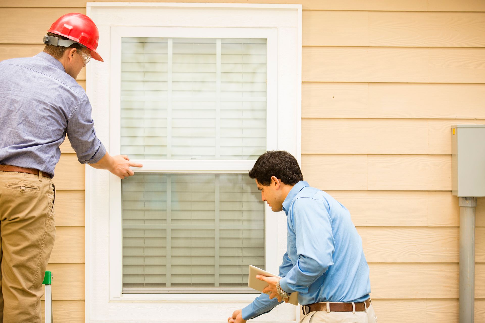 Two men inspecting a window on the exterior of a house.