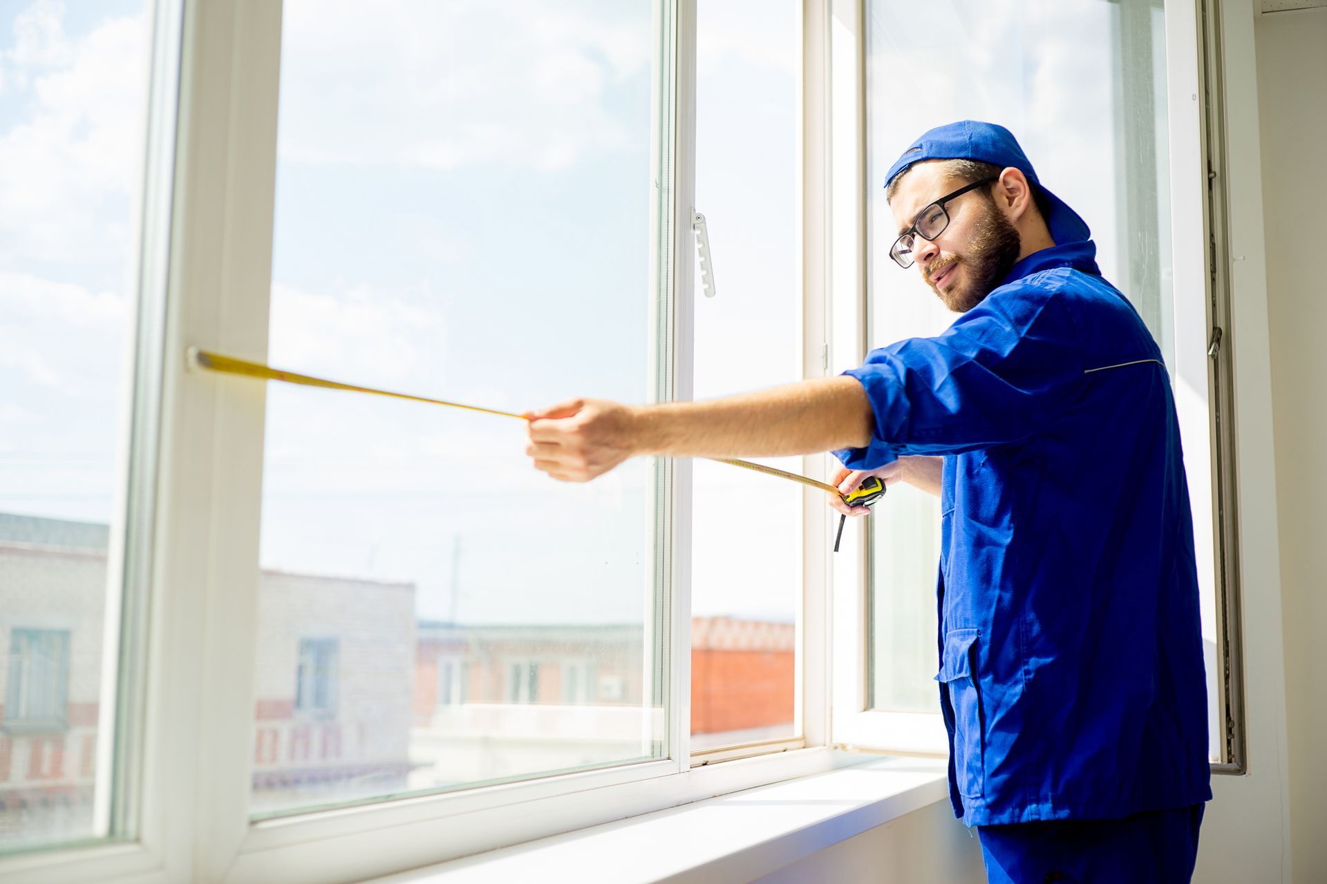 Window replacement company worker using tape measure on window frame for window replacement.