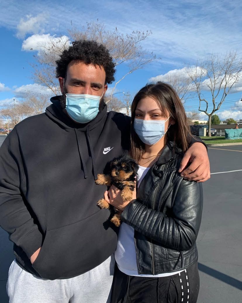 A man and a woman wearing face masks are holding a puppy.