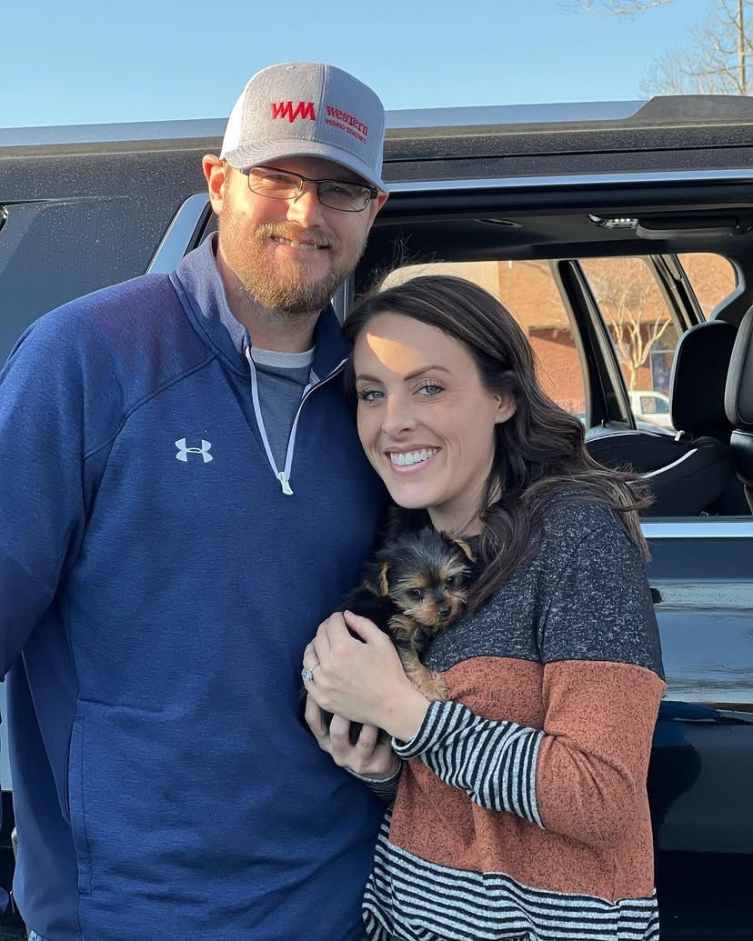 A man and a woman are holding a puppy in front of a car.