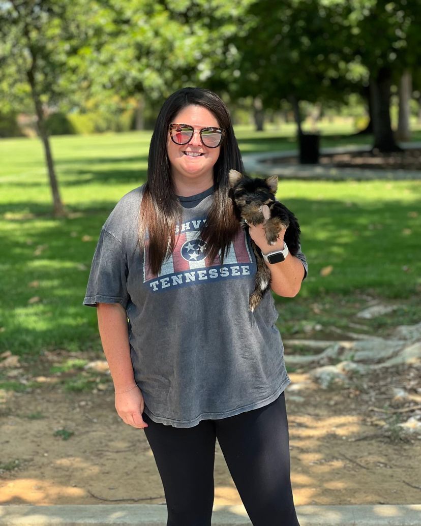 A woman is holding a small dog in her arms in a park.