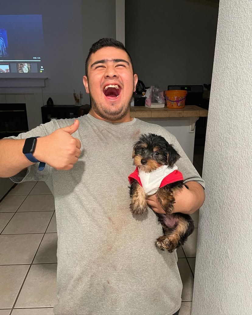 A man is holding a small dog in his arms and giving a thumbs up.