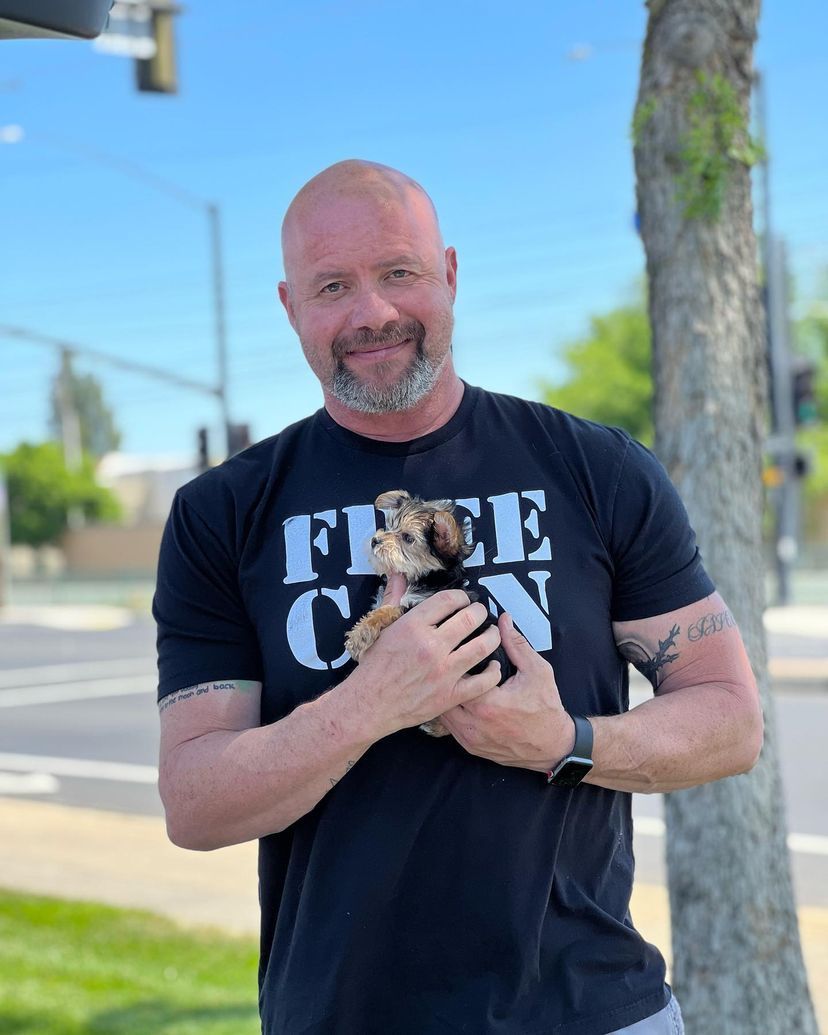 A man wearing a free con t-shirt is holding a small dog.