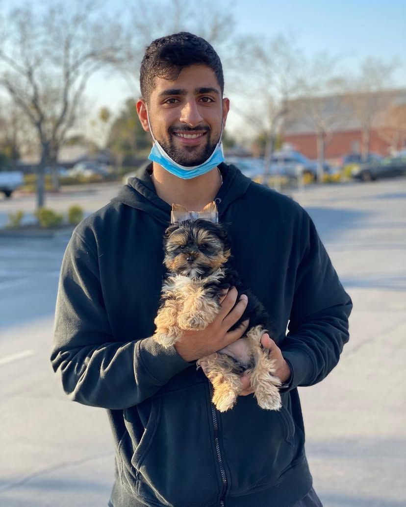A man wearing a mask is holding a small dog in his arms.