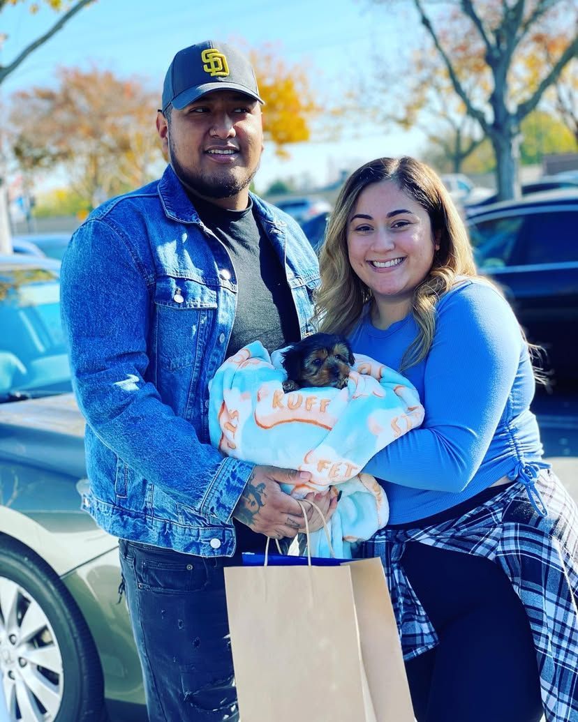 A man and a woman are holding a small dog in a parking lot.