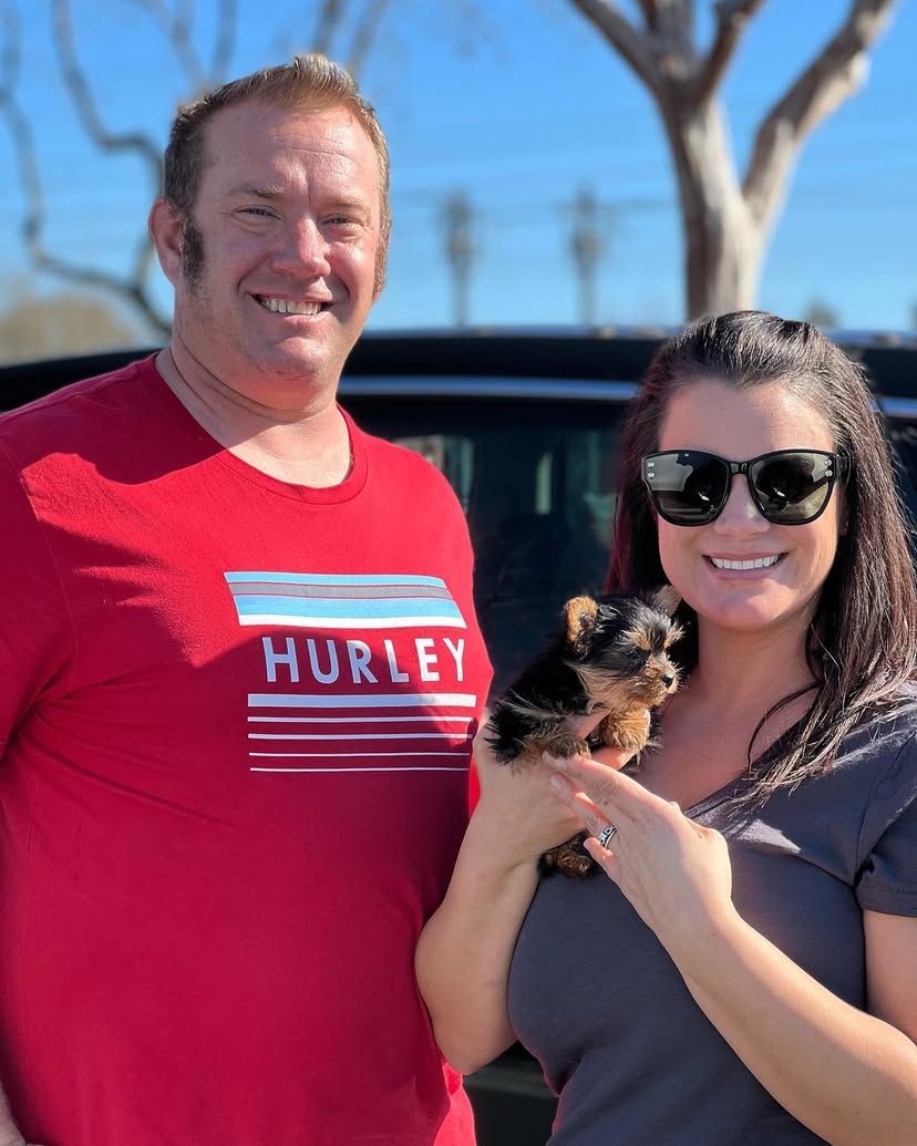 A man wearing a hurley shirt is standing next to a woman holding a small dog