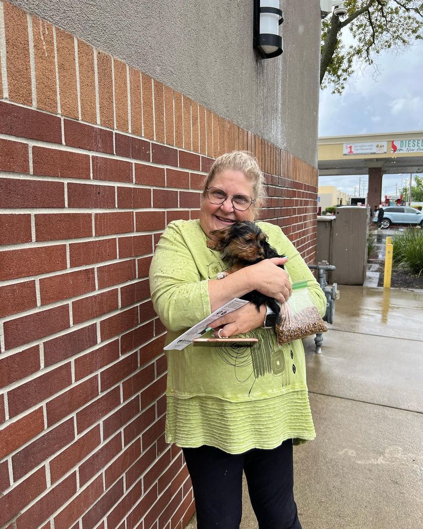 A woman is holding a small dog in front of a brick wall.