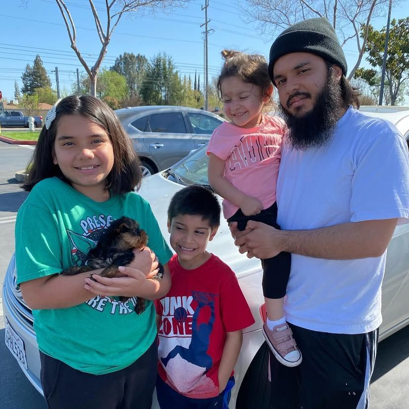 A man with a beard is holding a puppy with two children standing next to him