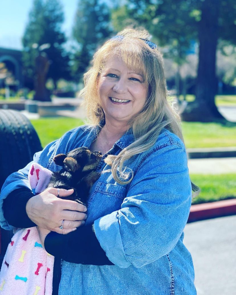 A woman is holding a small dog in her arms and smiling.
