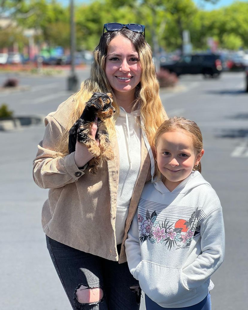 A woman and a little girl are standing next to each other holding a small dog.