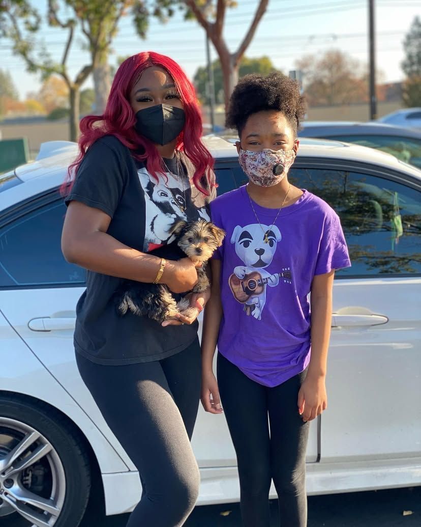 A woman and a girl wearing face masks are standing in front of a car.