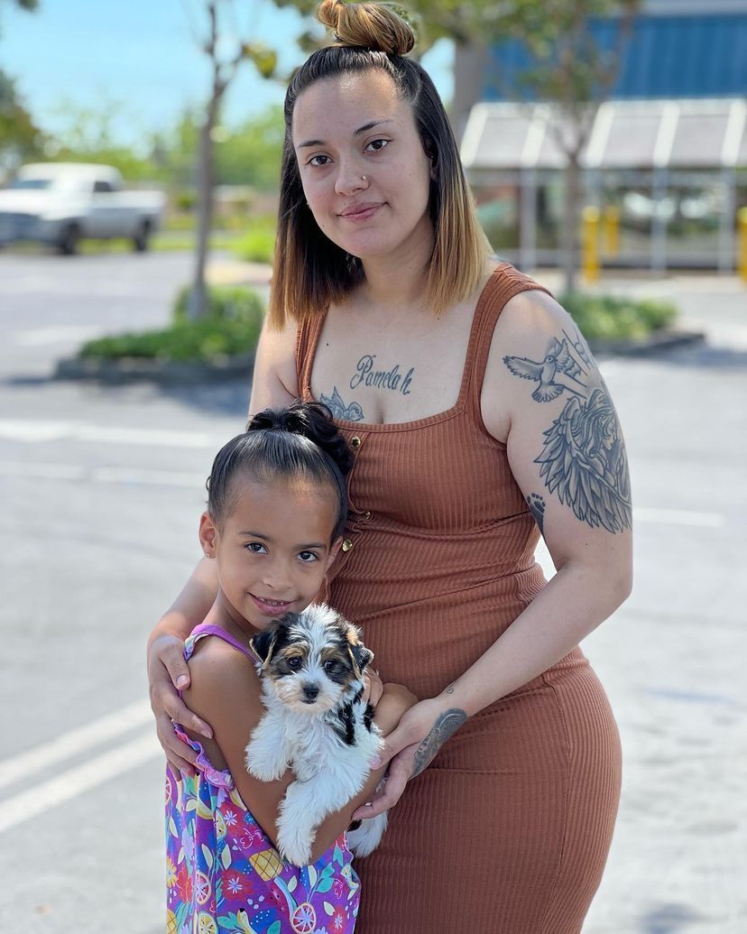 A woman and a little girl are holding a puppy in a parking lot.