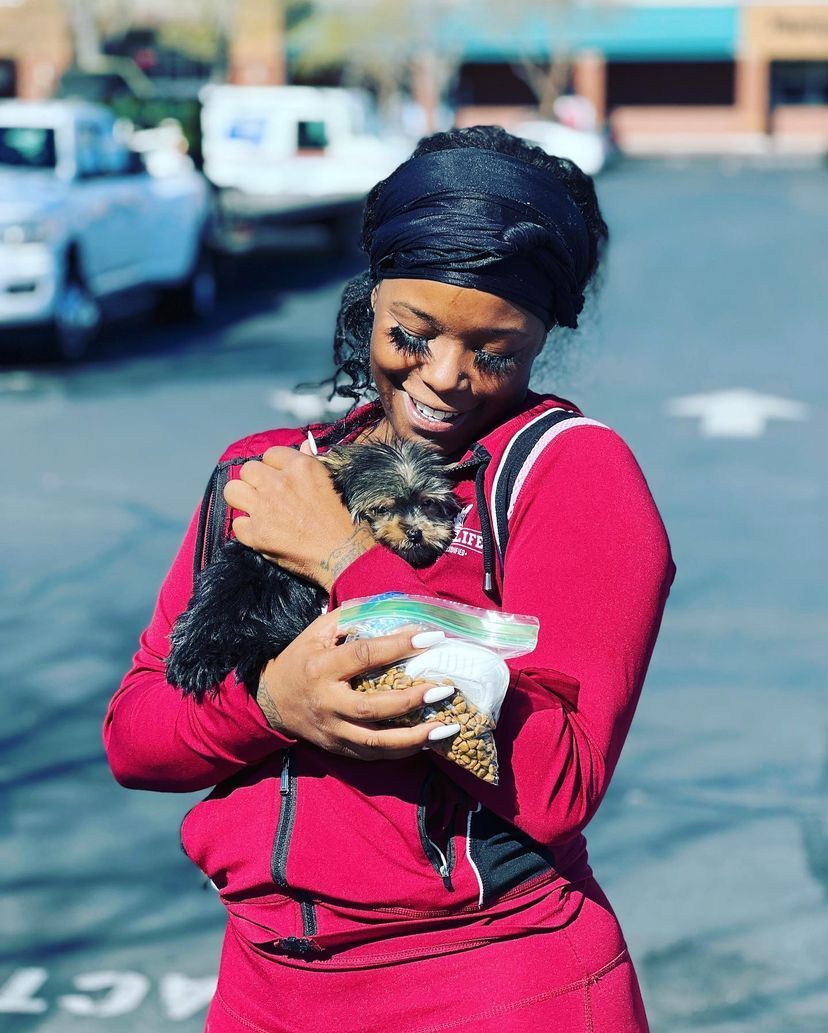 A woman in a red jacket is holding a small dog in her arms.