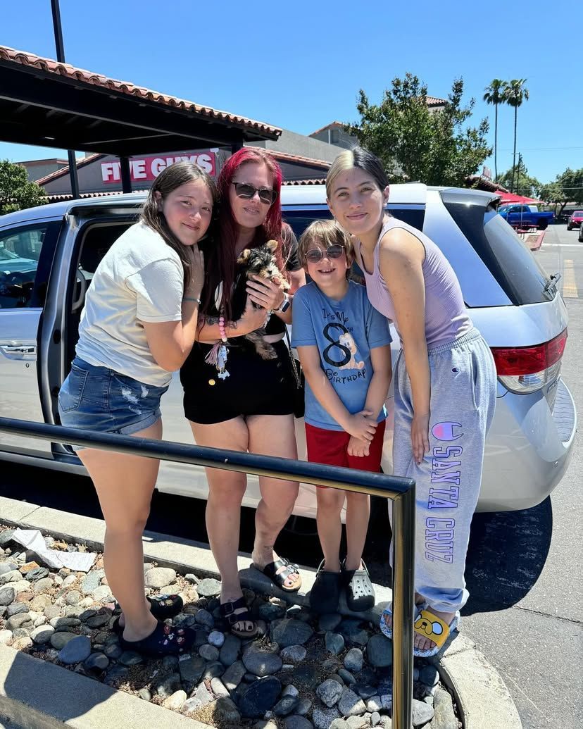 A group of people are posing for a picture in front of a car.
