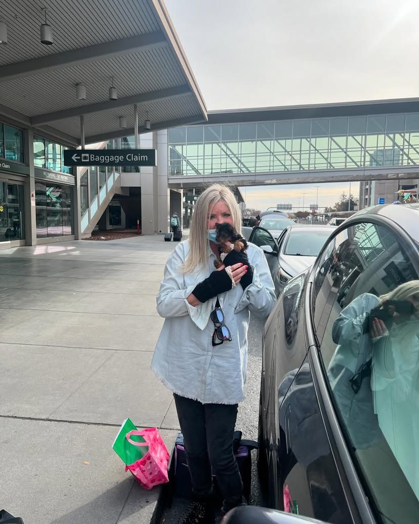 A woman is standing next to a car holding a puppy.