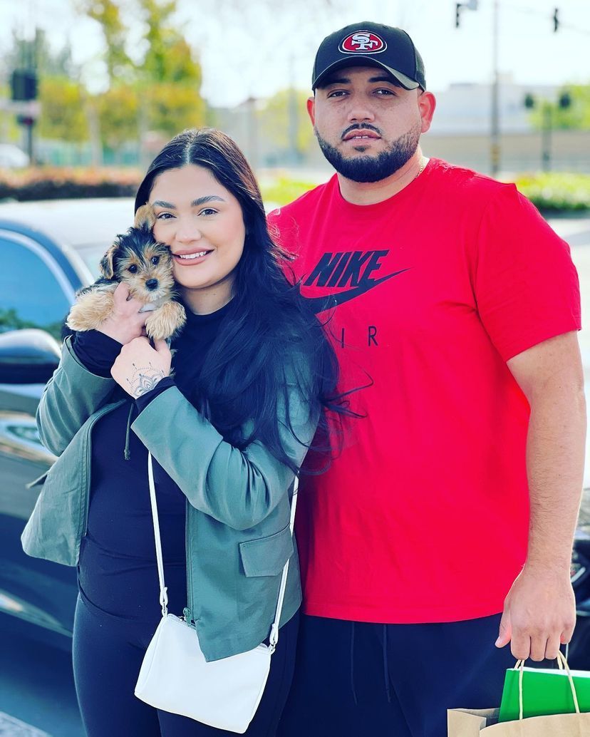 A man in a red nike shirt is standing next to a woman holding a puppy.