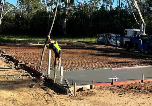 A Man Is Pouring Concrete Into A Hole In The Ground — Hinterland Concreting Pty Ltd In Lennox Head, NSW