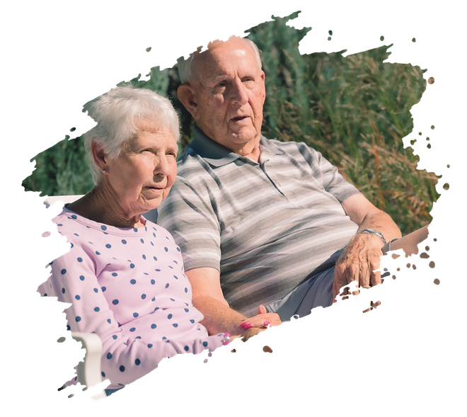 Elderly couple smiling and embracing on a park bench, joyful expressions, sunny outdoor setting.