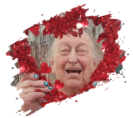 Elderly person laughing, framed by red tinsel and heart decorations, holding tinsel, blue nail polish.
