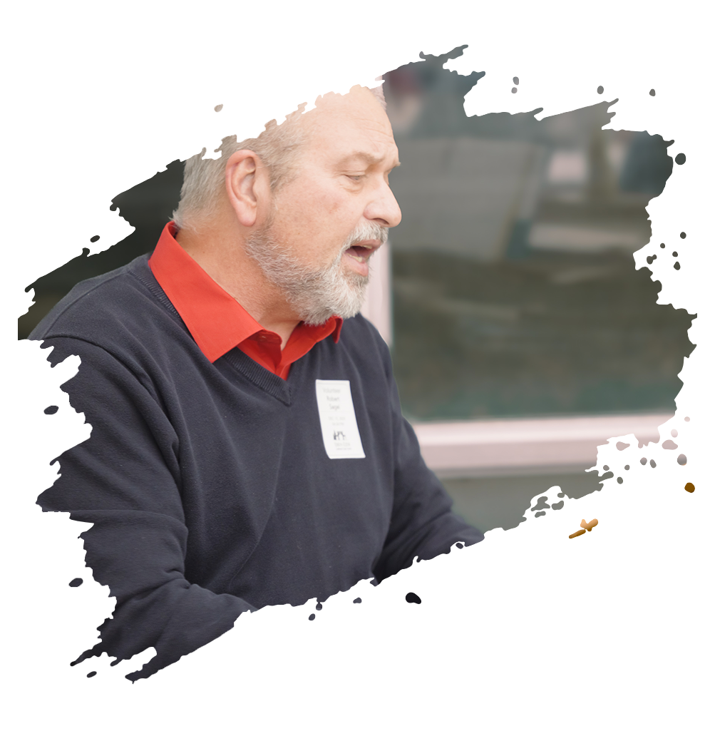 Brick church building with arched windows, a tree, and a white bench on a grassy area.