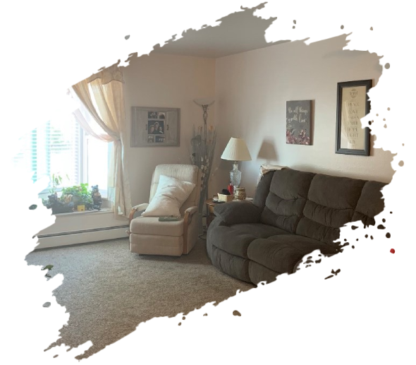 Cozy living room with recliner and sofa, curtains, and artwork. Soft lighting and neutral colors.