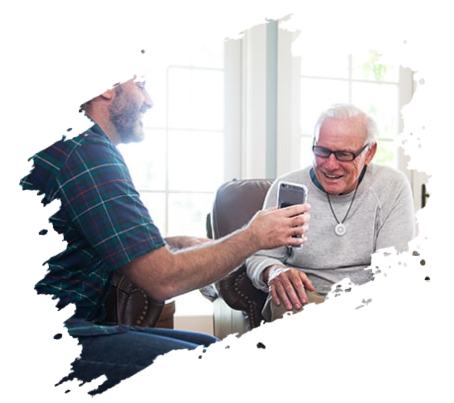 Man shows a smartphone to an older man. Both are smiling in a living room setting.