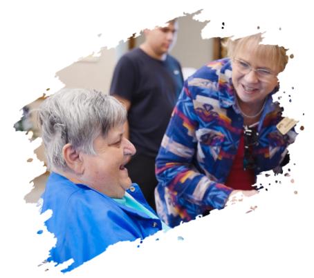 Two women smiling, interacting, inside, another person behind them.