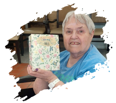 Smiling senior woman holding a floral-covered book, indoors. She wears a blue shirt and has a white wristband.