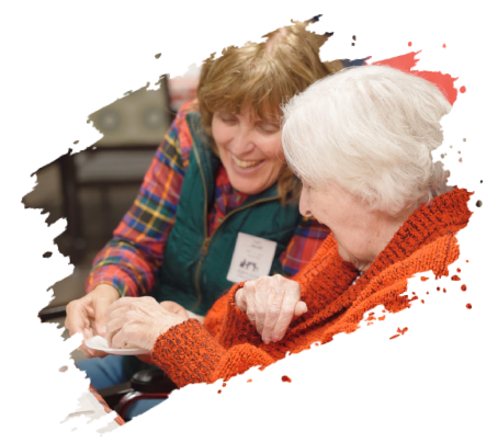 Woman helping elderly woman with paper; both smiling indoors.