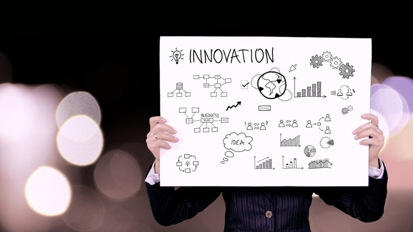 Person holding a white board with “Innovation” and hand-drawn business diagrams on a blurred dark background