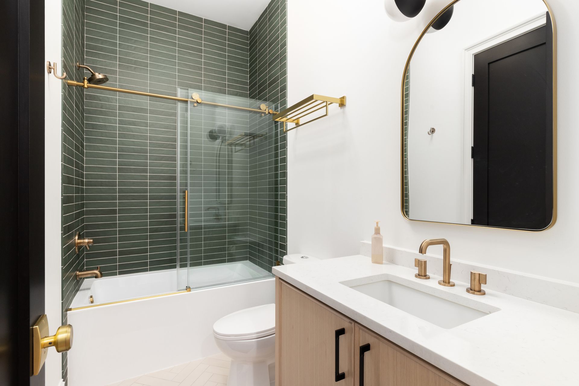 View of a completed bathroom remodeling with gold accents and a shower with green tiles.