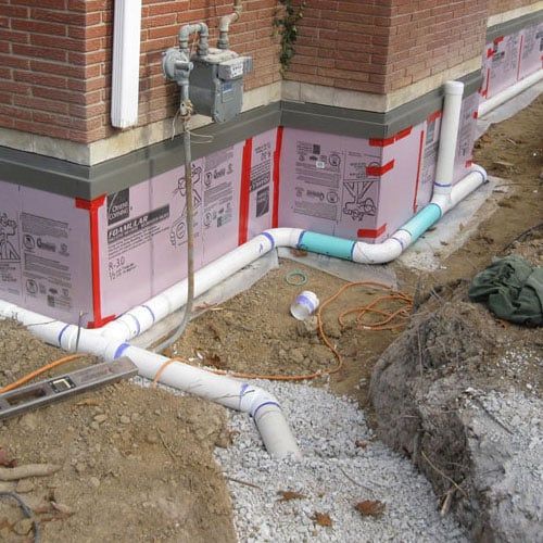 A Drainage System Is Being Installed on The Side of A Brick Building — Columbia, MO — Naugle Construction Company