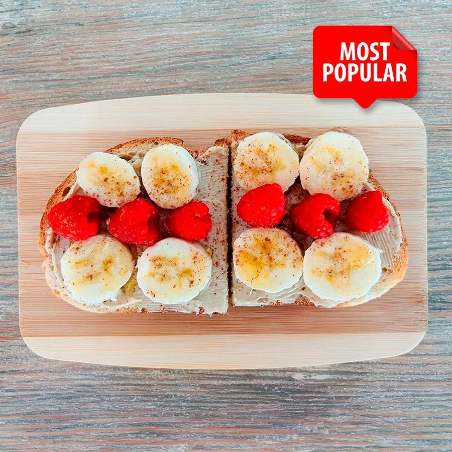 Two slices of toast with bananas and raspberries on a wooden cutting board