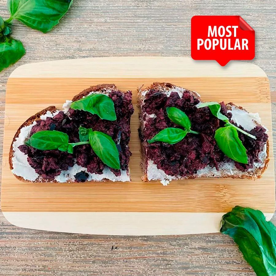 Two slices of bread with olives and basil on a wooden cutting board.