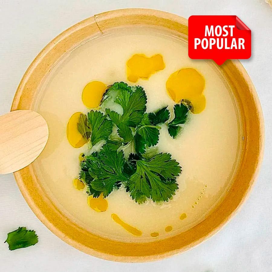 A bowl of soup with cilantro and a wooden spoon in it.