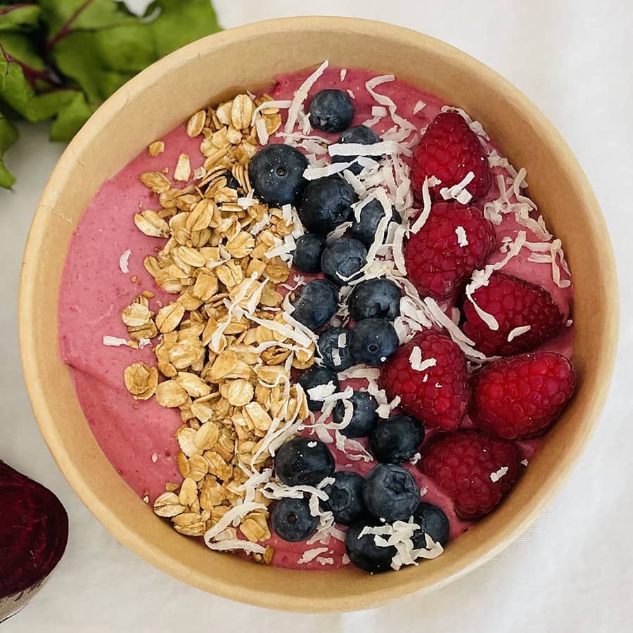A bowl of smoothie with raspberries , blueberries , granola and coconut.