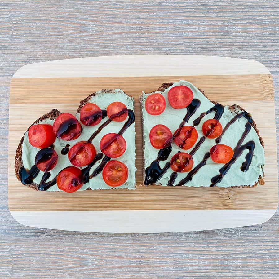 Two slices of toast with avocado and tomatoes on a wooden cutting board.