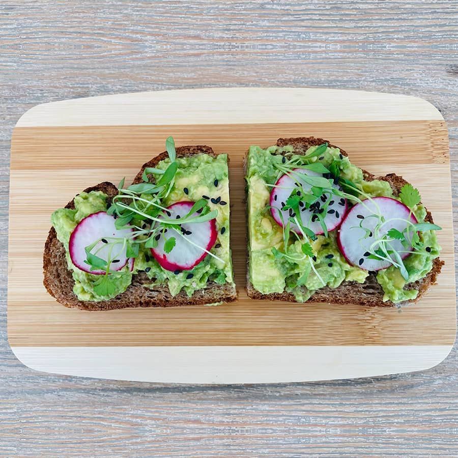 Two slices of avocado toast with radishes on a wooden cutting board.