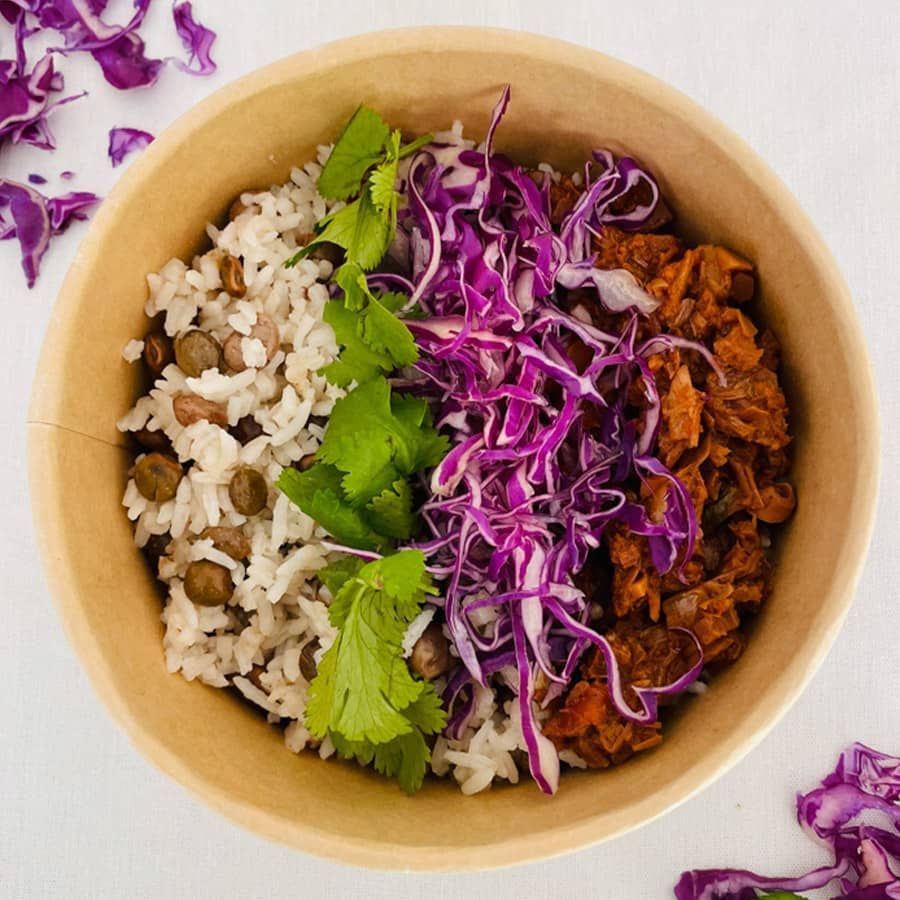 A bowl of food with rice beans and cabbage on a table