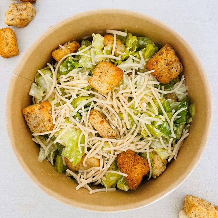 A bowl of caesar salad with croutons and cheese on a table.