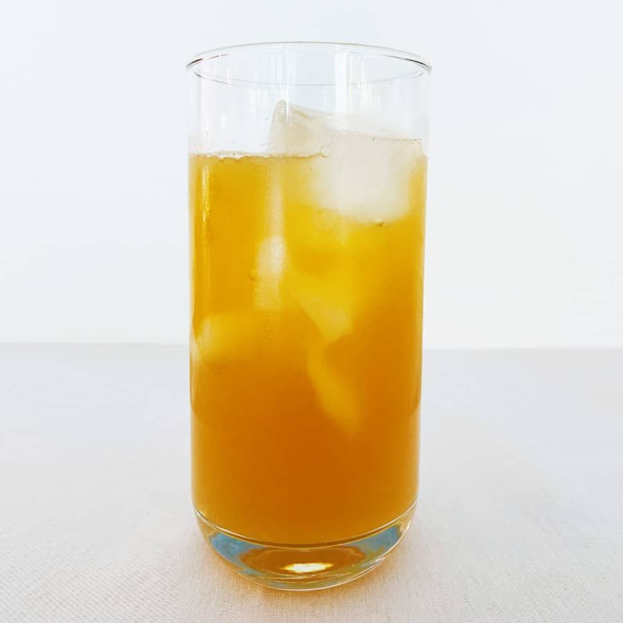 A glass of orange juice with ice cubes on a table.