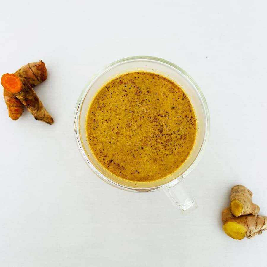 A cup of soup next to a piece of turmeric.
