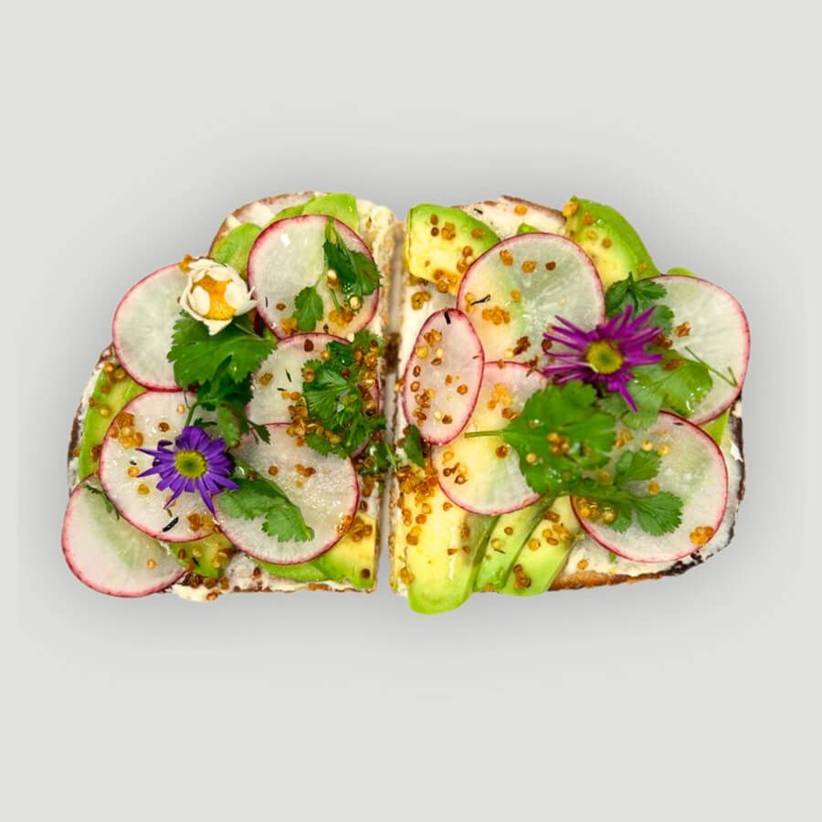Two slices of avocado toast with radishes on a wooden cutting board.