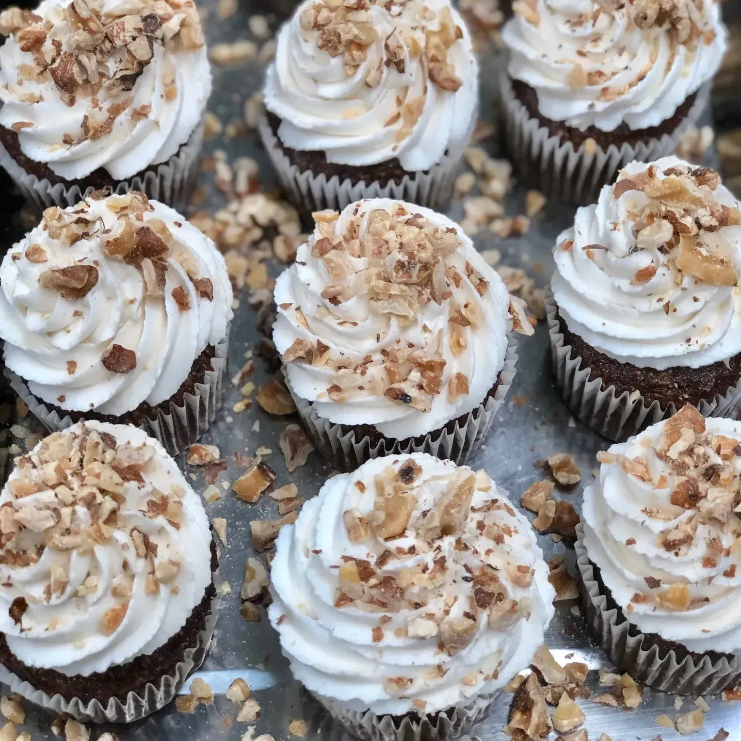 A bunch of cupcakes with white frosting and walnuts on top