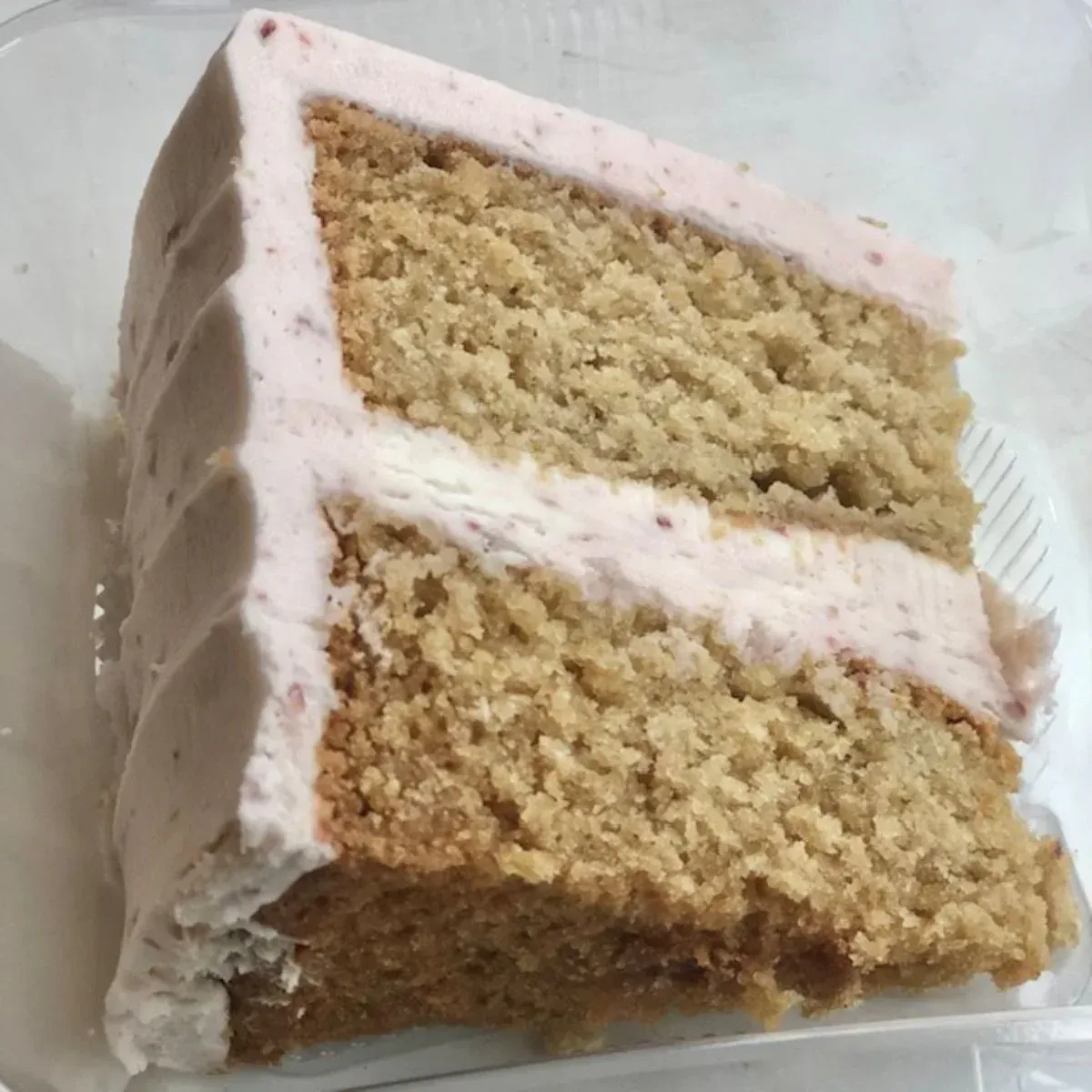 A slice of cake with pink frosting in a plastic container