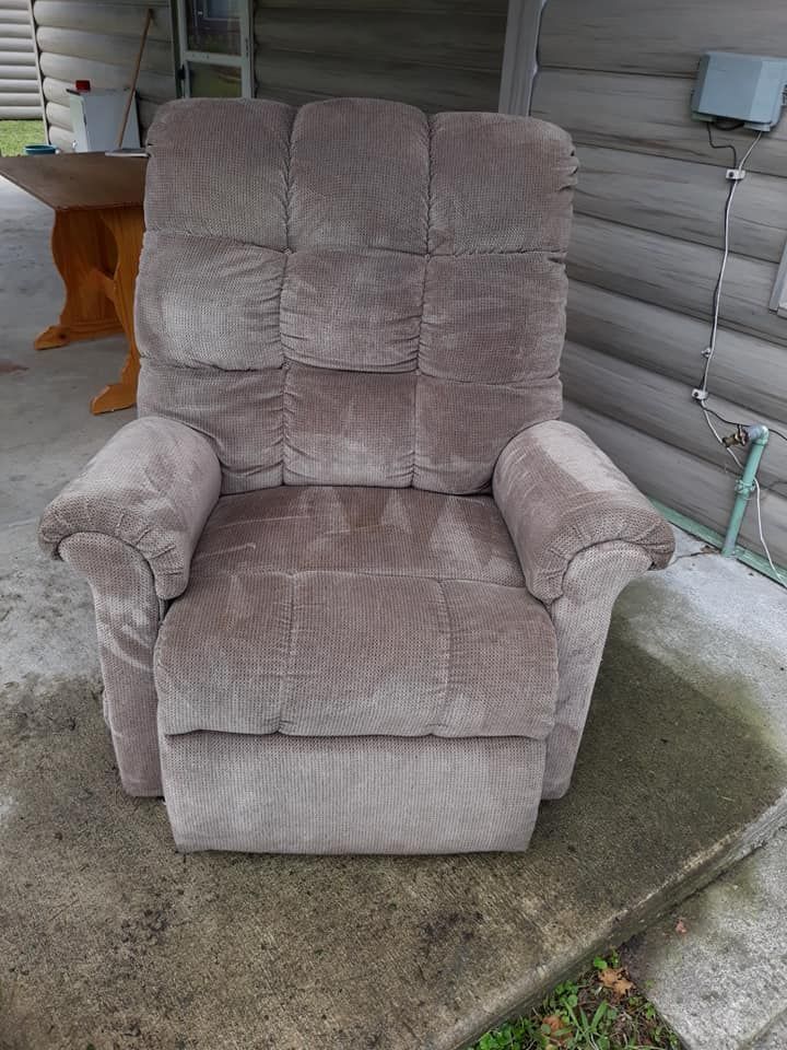 Brown upholstered recliner chair on a concrete porch, with a metal railing in the background