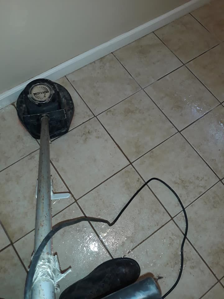 Floor buffer cleaning beige tile floor in a corner near a white baseboard.